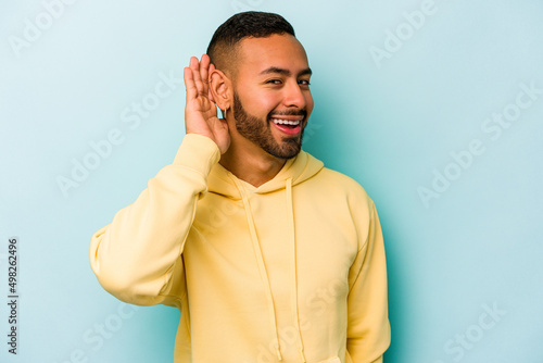 Young hispanic man isolated on blue background trying to listening a gossip.