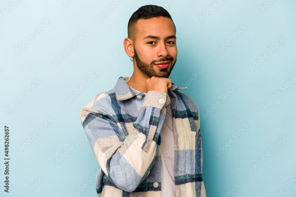 Young hispanic man isolated on blue background smiling happy and confident, touching chin with hand. Young hispanic man isolated on blue background smiling happy and confident, touching chin with hand.