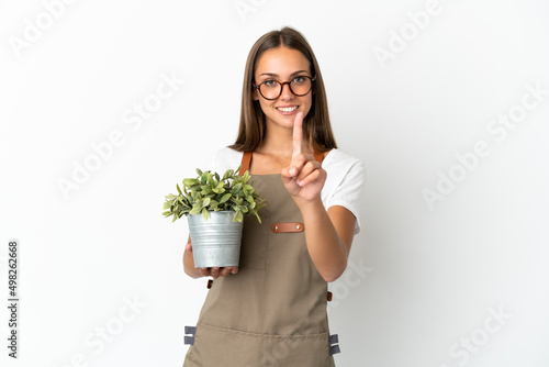 Gardener girl holding a plant over isolated white background showing and lifting a finger