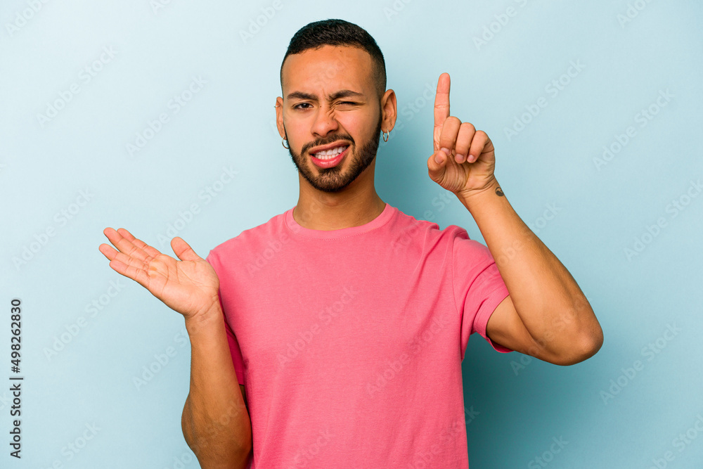 Fototapeta premium Young hispanic man isolated on blue background holding and showing a product on hand.