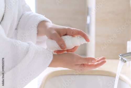 .Woman in the robe applying cream after washing hands for protective and care dry skin near white sink in bathroom with sunlight from the window.