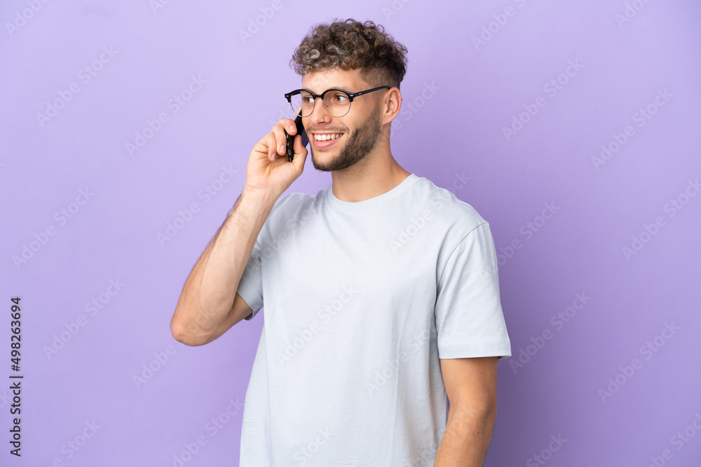 Delivery caucasian man isolated on purple background keeping a conversation with the mobile phone Delivery caucasian man isolated on purple background keeping a conversation with the mobile phone