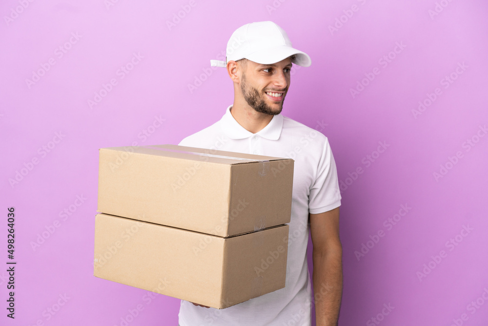 Delivery caucasian man isolated on purple background looking to the side and smiling Delivery caucasian man isolated on purple background looking to the side and smiling