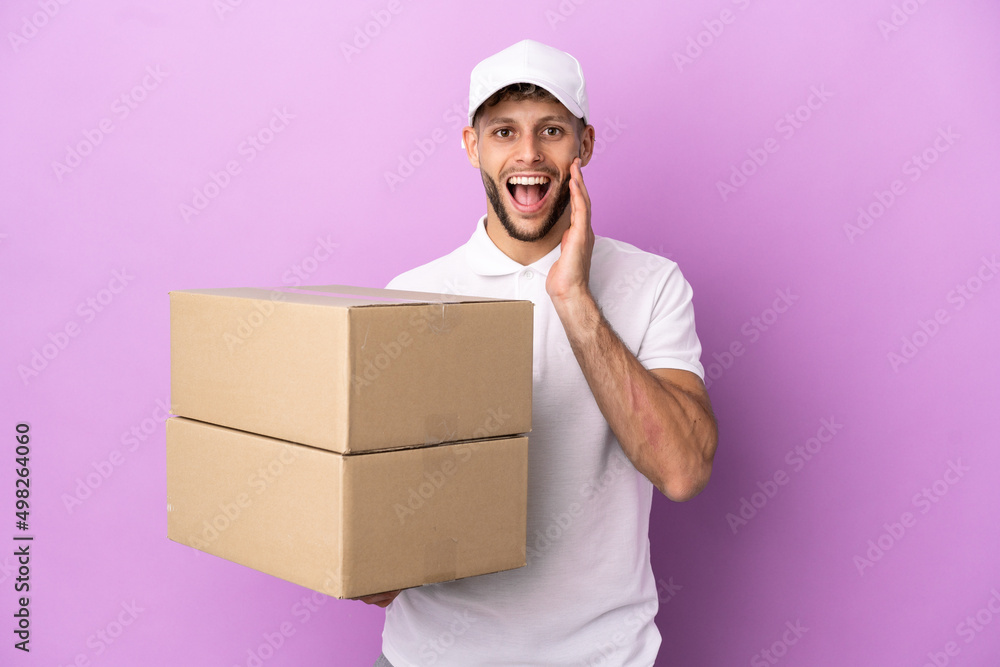 Delivery caucasian man isolated on purple background with surprise and shocked facial expression Delivery caucasian man isolated on purple background with surprise and shocked facial expression