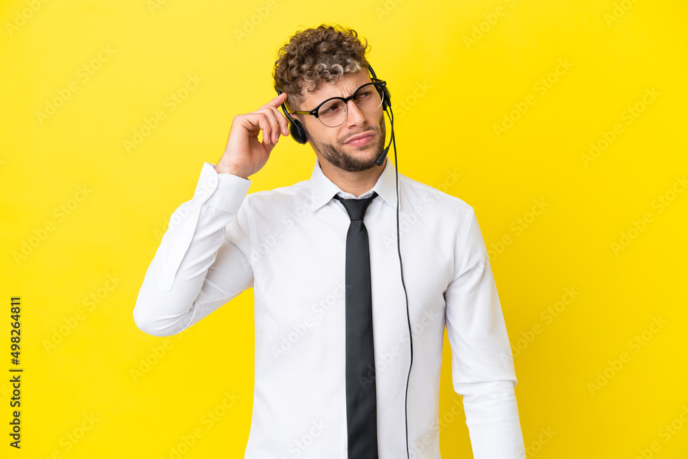 Telemarketer blonde man working with a headset isolated on yellow background having doubts and with confuse face expression Telemarketer blonde man working with a headset isolated on yellow background having doubts and with confuse face expression