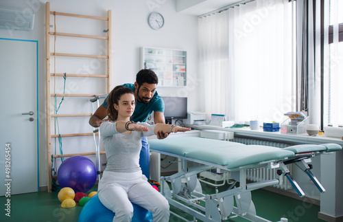 Young male physiotherapist exercising with young woman patient on ball in a physic room photo