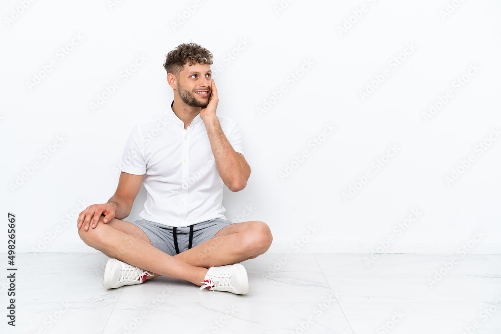 Young blonde man sitting on the floor isolated on white background thinking an idea