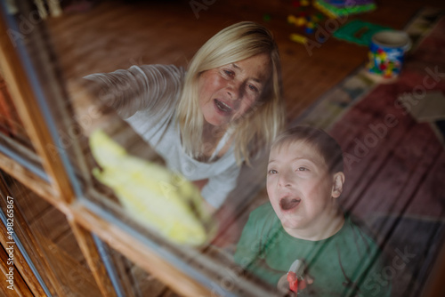 Boy with Down syndrome with his grandmother cleaning window at home.