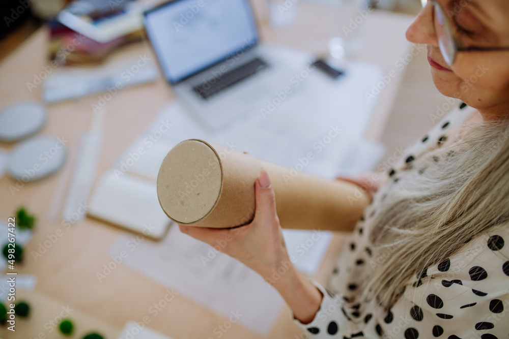 Close-up of woman architect pulling rolled-up blueprints out of tube in office.