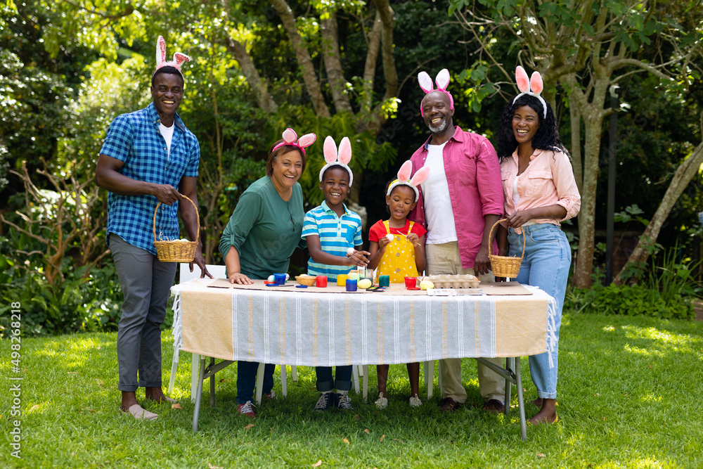 Naklejka premium Happy african american multigenerational family in bunny ears with easter eggs in backyard