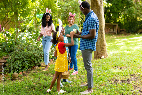 Happy african american siblings wearing bunny ears with family in backyard on easter day