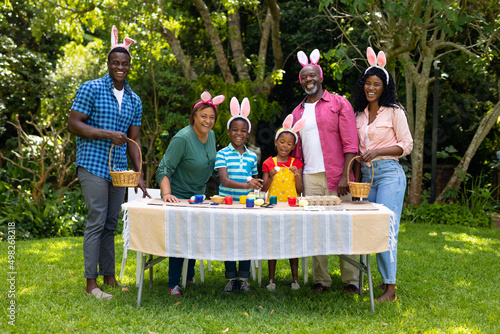 Happy african american multigenerational family in bunny ears with easter eggs in backyard
