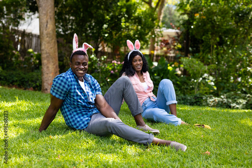 Portrait of happy african american mid adult couple wearing bunny ears while sitting in backyard