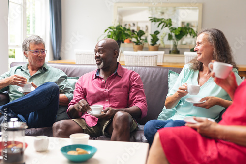 Multiracial senior female and male friends talking while having coffee together at home