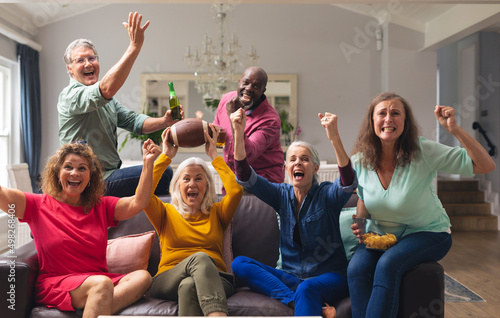 Multiracial senior male and female friends cheering while watching rugby match on tv at home