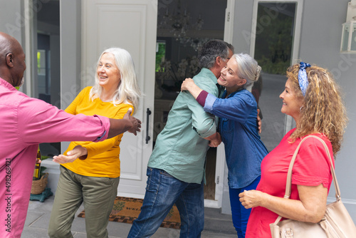 Happy senior multiracial friends greeting each other at entrance during house party
