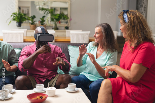 Multiracial senior women and man with male friend using vr headset at home