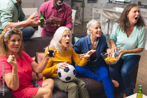 Shocked multiracial senior male and female friends watching soccer match on tv at home