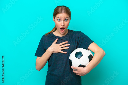 Young football player woman isolated on blue background surprised and shocked while looking right © luismolinero