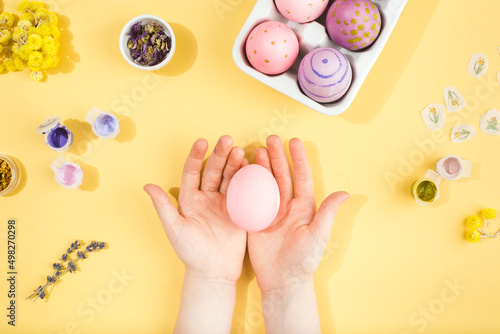 Child hands decorate Easter eggs on yellow background. Happy easter concept.