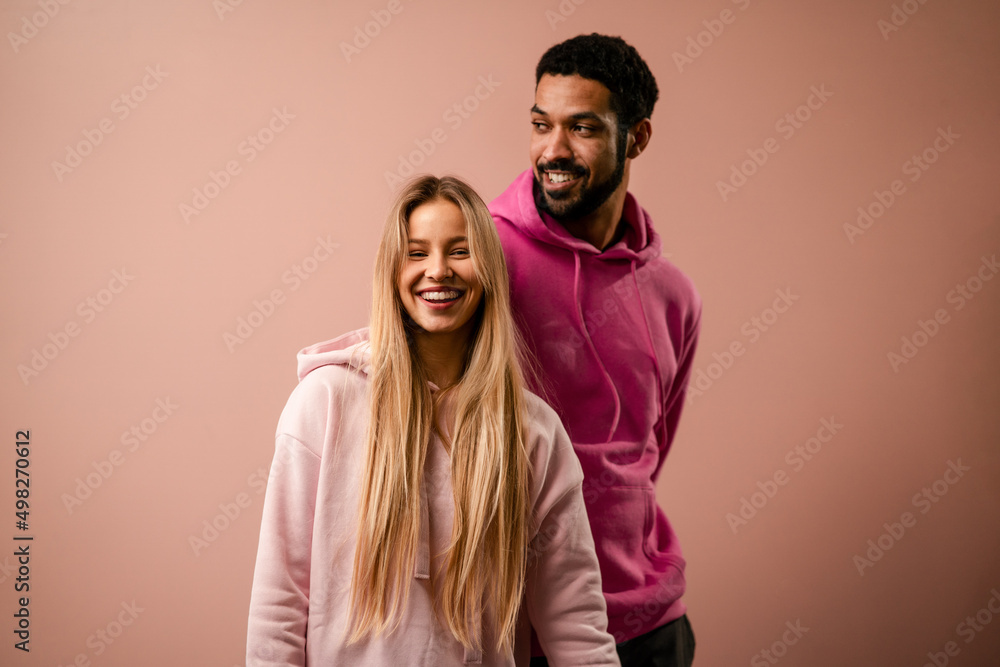 Obraz premium Fashion studio portrait of a happy young couple in hoodie posing over pink background.