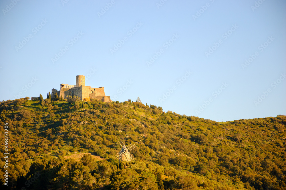Dry weather. Fort Saint-Elme and old windmill on a hilltop at sunset. View from Collioure town. Pyrenees-Orientales department. South of France