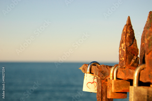 Love locks with hearts attached to spiky rusty fence of antique lighthouse in Collioure, France. Old love concept. Eternal love promise, hope concepts. © Elena Dijour