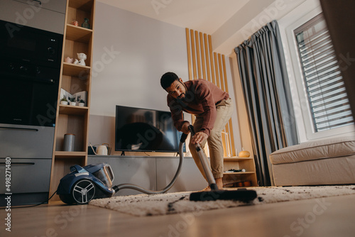 Fotografía Young man hoovering carpet with vacuum cleaner in living room