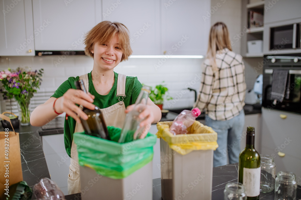 Teen girl throwing glass bottles in recycling bin in the kitchen. Teen girl throwing glass bottles in recycling bin in the kitchen.