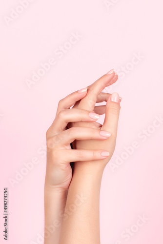 Female hands with beautiful natural manicure - pink nude nails on pink background. Nail care concept
