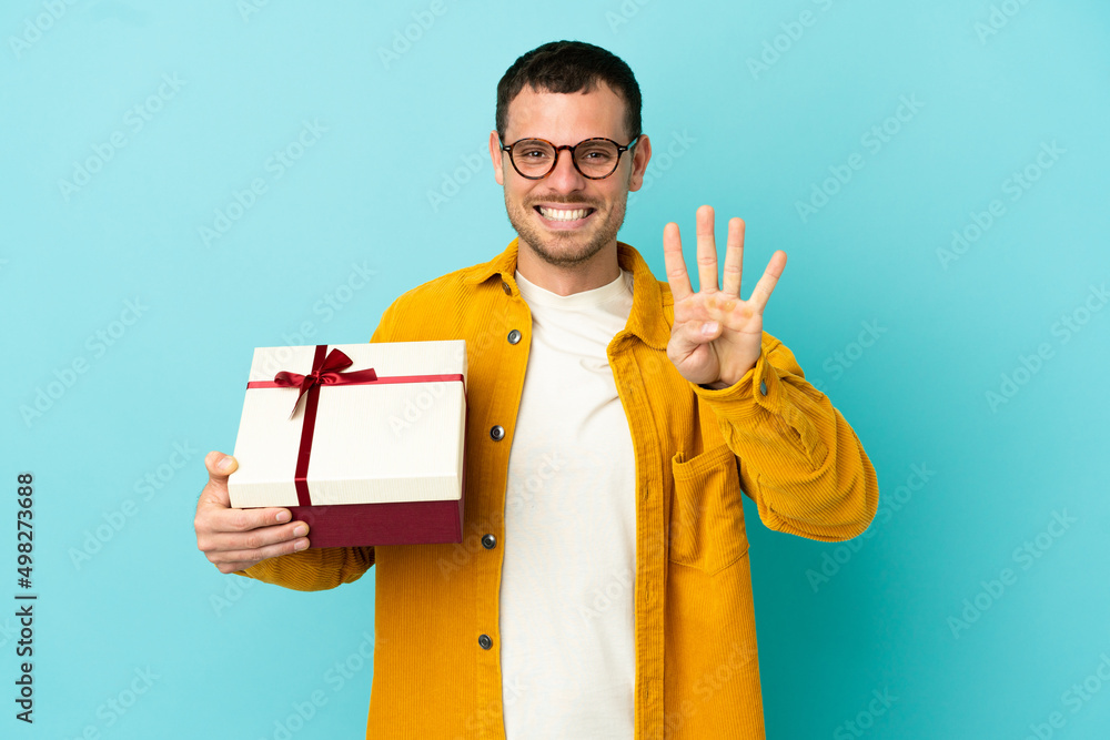 Brazilian man holding a gift over isolated blue background happy and counting four with fingers Brazilian man holding a gift over isolated blue background happy and counting four with fingers