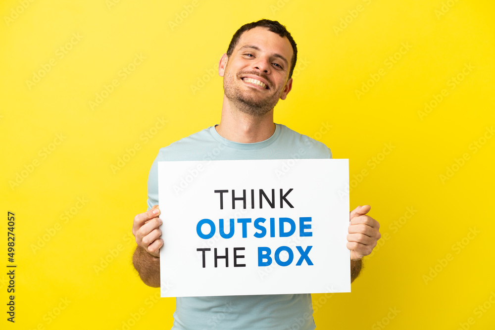 Brazilian man over isolated purple background holding a placard with text Think Outside The Box Brazilian man over isolated purple background holding a placard with text Think Outside The Box