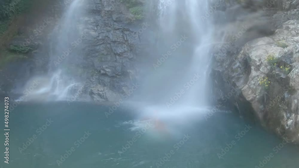 young man jumping in waterfall from cliff at morning from flat angle young man jumping in waterfall from cliff at morning from flat angle