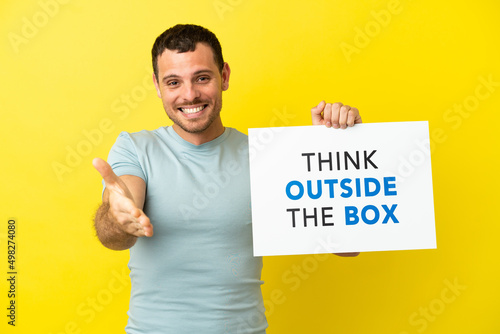 Brazilian man over isolated purple background holding a placard with text Think Outside The Box making a deal © luismolinero
