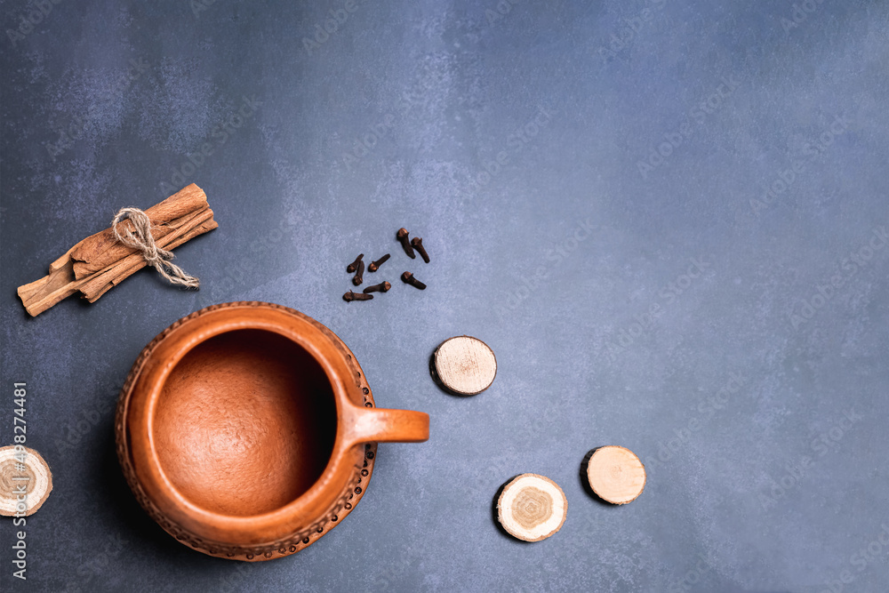 Red clay mug on a saucer. Top view, location at the bottom left in the corner. Cinnamon, cloves and sticks arranged around on a grey monotone background
