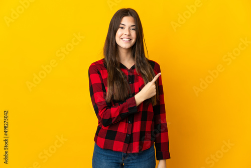 Teenager Brazilian girl isolated on yellow background pointing to the side to present a product