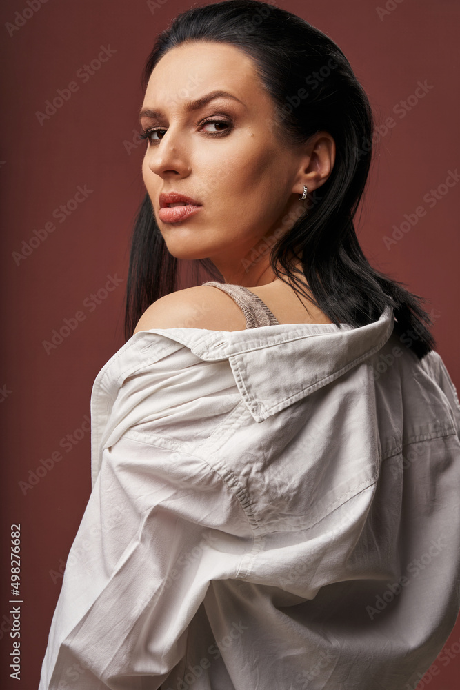a beautiful woman with dark hair in a white shirt looks sternly over her shoulder a beautiful woman with dark hair in a white shirt looks sternly over her shoulder