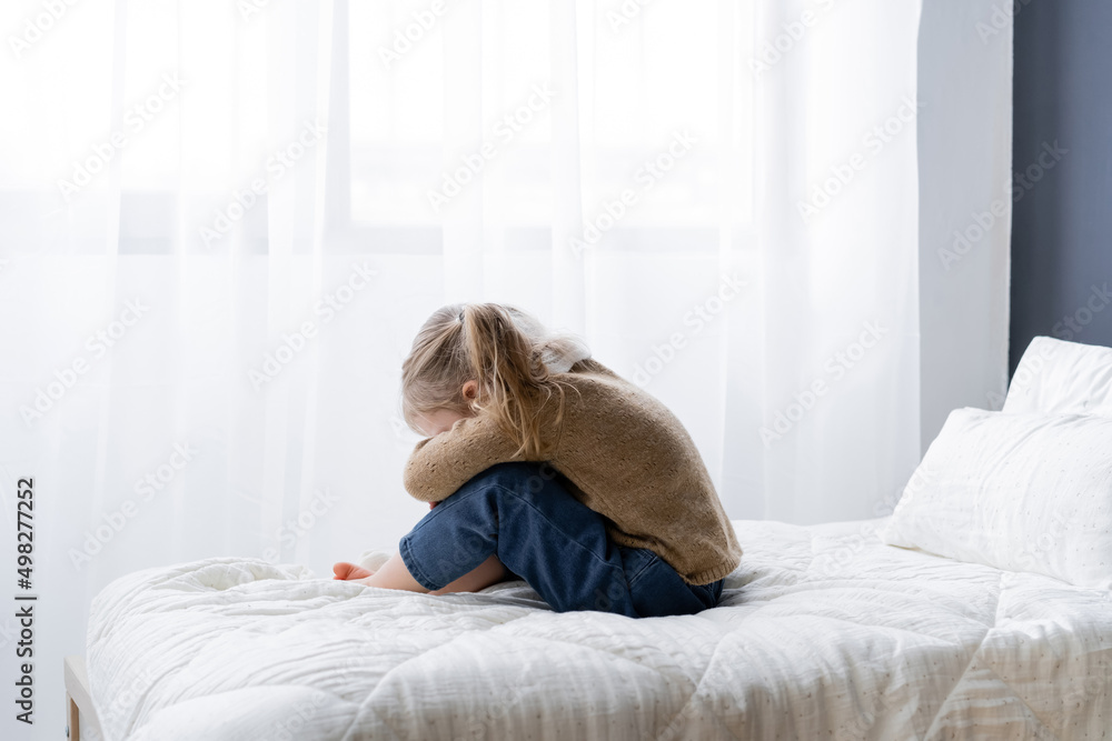 side view of upset girl obscuring face while sitting on bed at home. side view of upset girl obscuring face while sitting on bed at home.