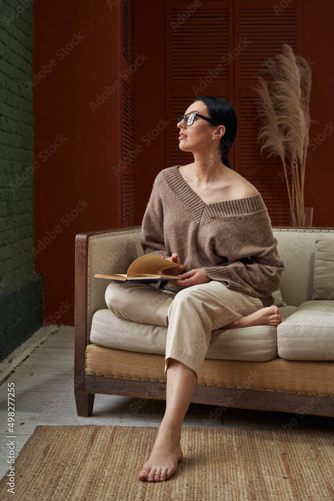 a beautiful woman with dark hair in cozy clothes sits on the sofa, tucking one leg up and holding in her hands. naturalness, naturalness a beautiful woman with dark hair in cozy clothes sits on the sofa, tucking one leg up and holding in her hands. naturalness, naturalness