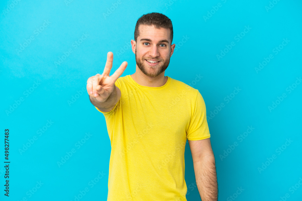 Young handsome caucasian man isolated on blue background smiling and showing victory sign Young handsome caucasian man isolated on blue background smiling and showing victory sign