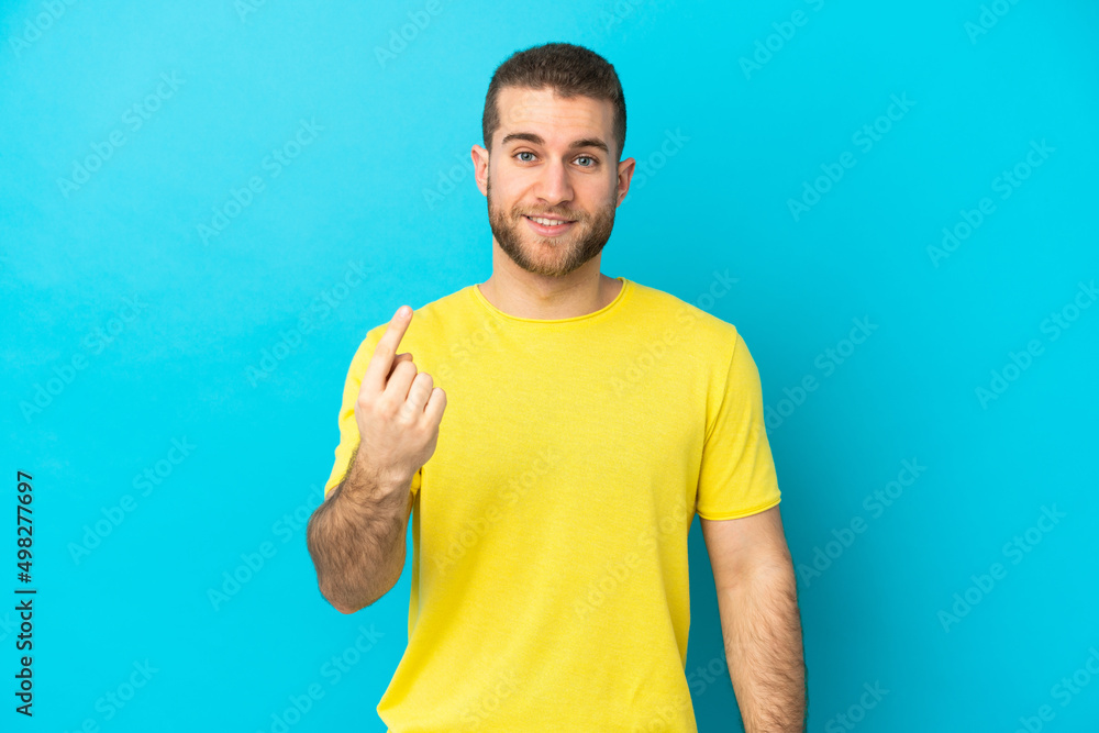 Young handsome caucasian man isolated on blue background doing coming gesture