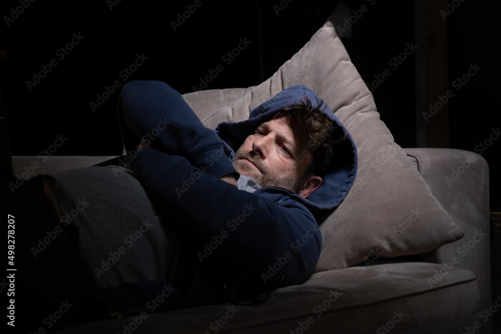 Senior Mann mit Migräne oder Depressionen hat sich einsam im dunkeln auf seine Couch zurück gezogen. Senior Mann mit Migräne oder Depressionen hat sich einsam im dunkeln auf seine Couch zurück gezogen.