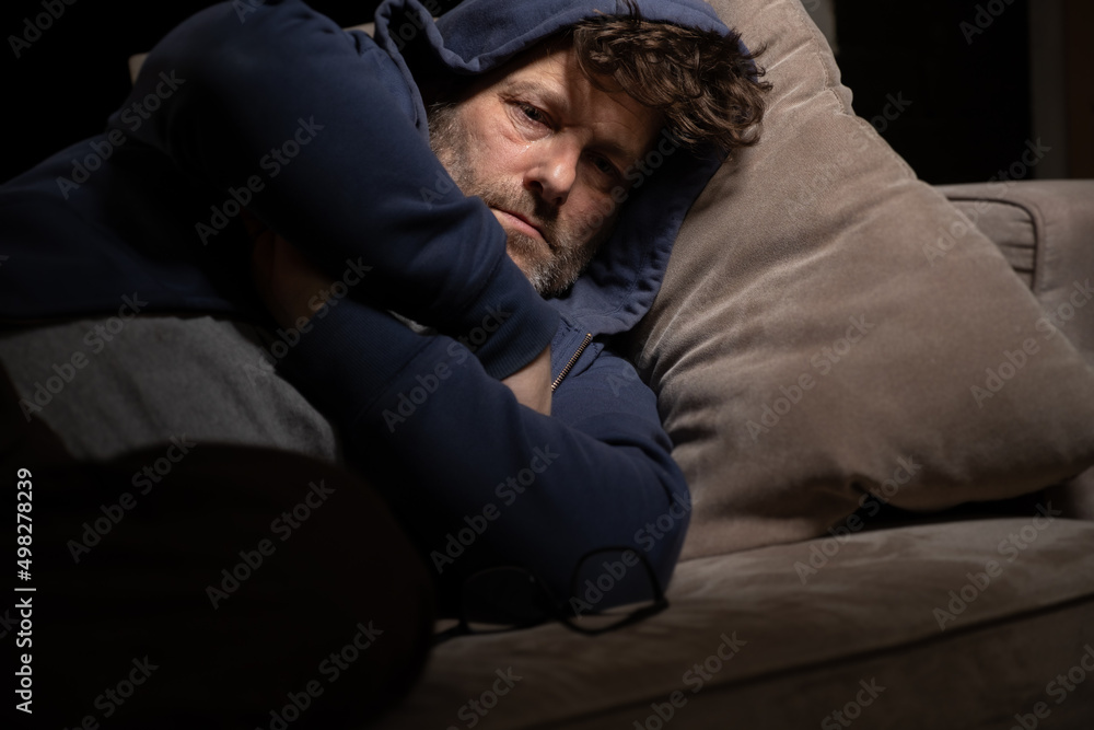 Fototapeta premium Senior Mann mit Migräne oder Depressionen hat sich einsam im dunkeln auf seine Couch zurück gezogen.