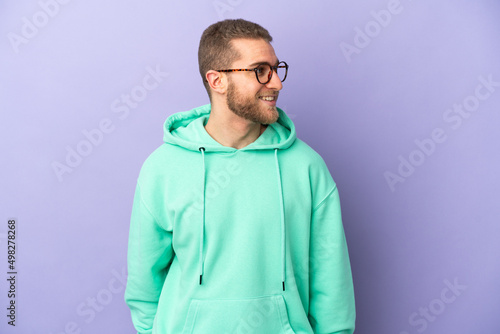 Young handsome caucasian man isolated on purple background looking to the side and smiling © luismolinero