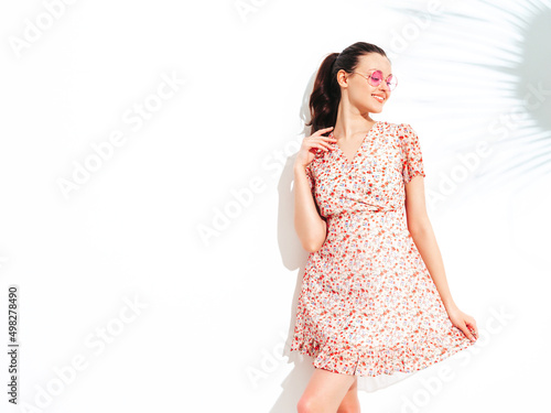Young beautiful smiling female in trendy summer dress. Sexy carefree woman posing near red wall in studio. Positive brunette model having fun and going crazy. Cheerful and happy