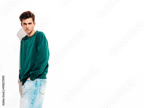 Portrait of handsome confident stylish hipster lambersexual model.Man dressed in green sweater and jeans. Fashion male posing in studio near white wall. Isolated