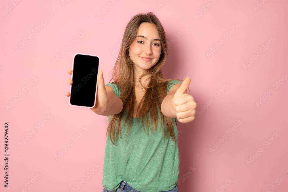 Stylish girl showing empty mobile phone screen and looking pleased, recommending application for smartphone, demonstrating shopping site over pink background Stylish girl showing empty mobile phone screen and looking pleased, recommending application for smartphone, demonstrating shopping site over pink background