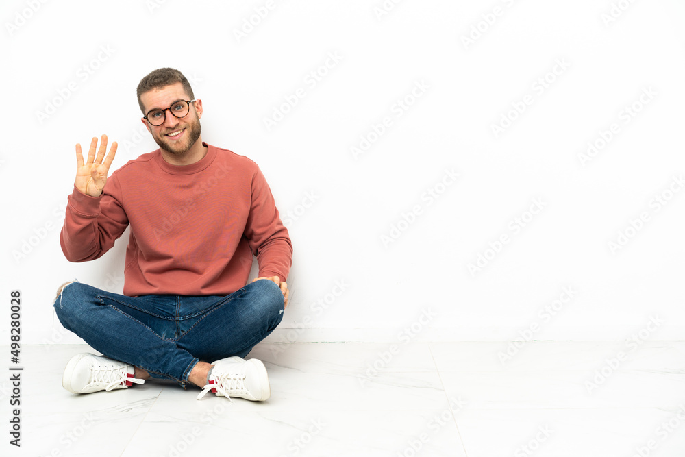 Young handsome man sitting on the floor happy and counting four with fingers Young handsome man sitting on the floor happy and counting four with fingers