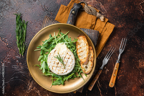 Salad with grilled Camembert cheese, arugula, toast and rosemary in a plate. Dark background. Top view
