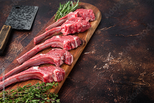 Raw Lamb chop steak on butcher board with rosemary and thyme. Dark background. Top view. Copy space